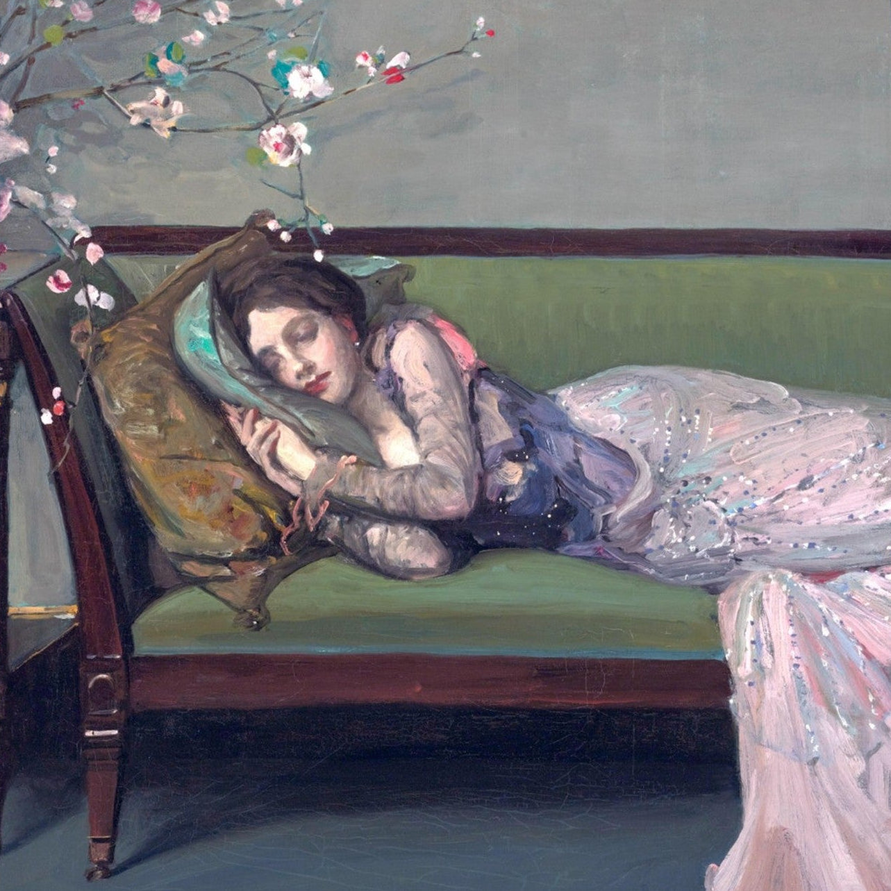 Woman in a pink dress lying on a green couch with flowers in her hair, in a room with a gray wall.